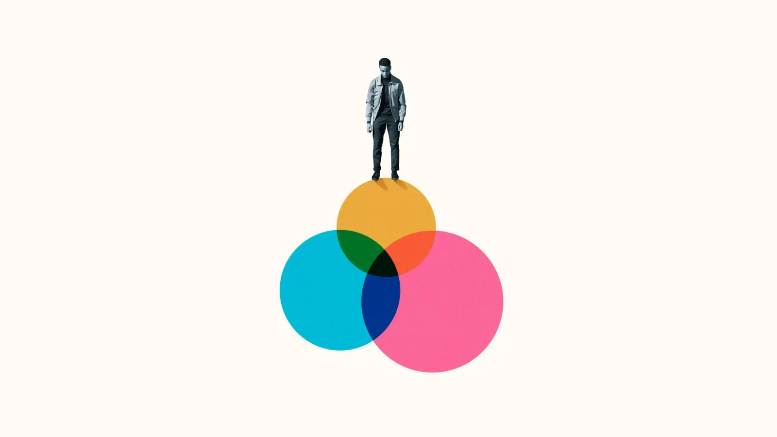 A young man standing on top of three overlapping translucent circles in yellow, cyan and pink, looking down at where they meet.