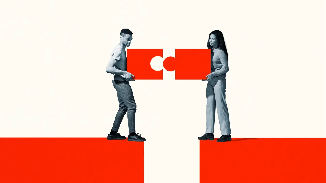 Two young people standing on facing red platforms across a gap, each holding half of a red puzzle piece so the two halves meet in the middle.
